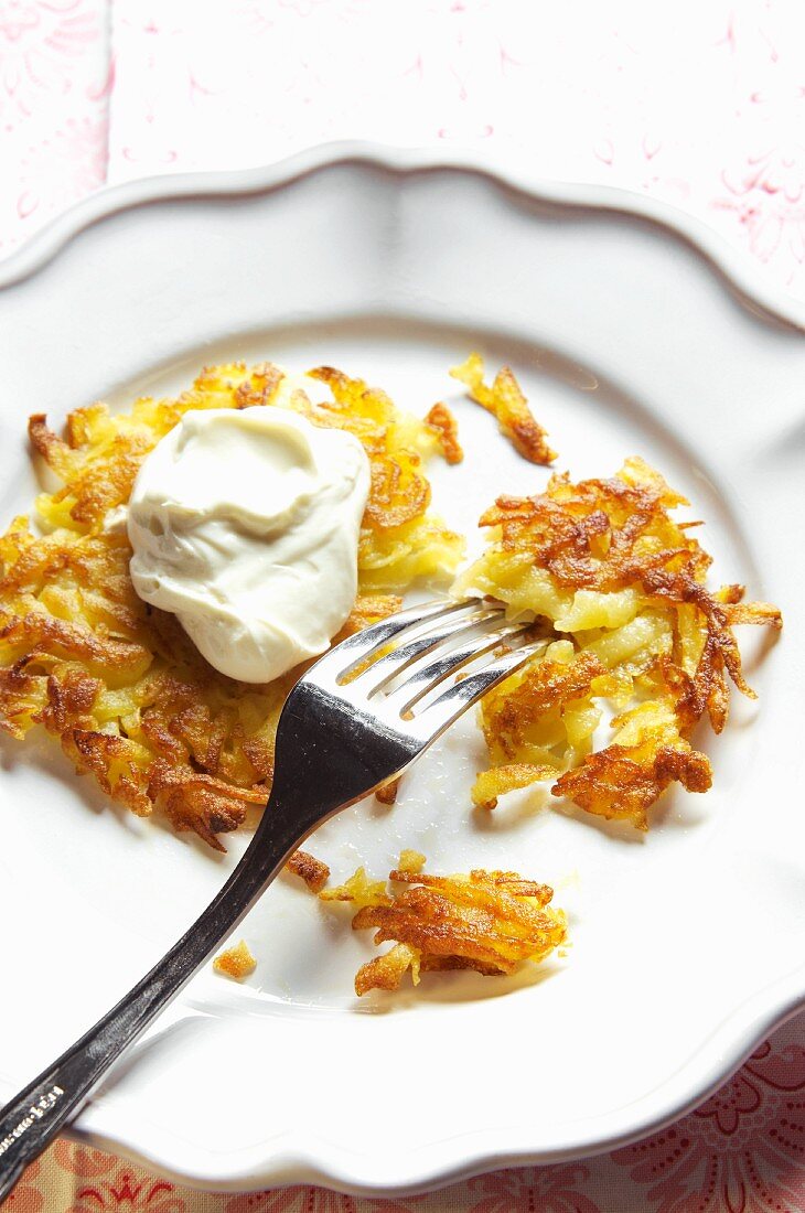 Kartoffelrösti mit Schmand, angebissen & mit Gabel auf Teller