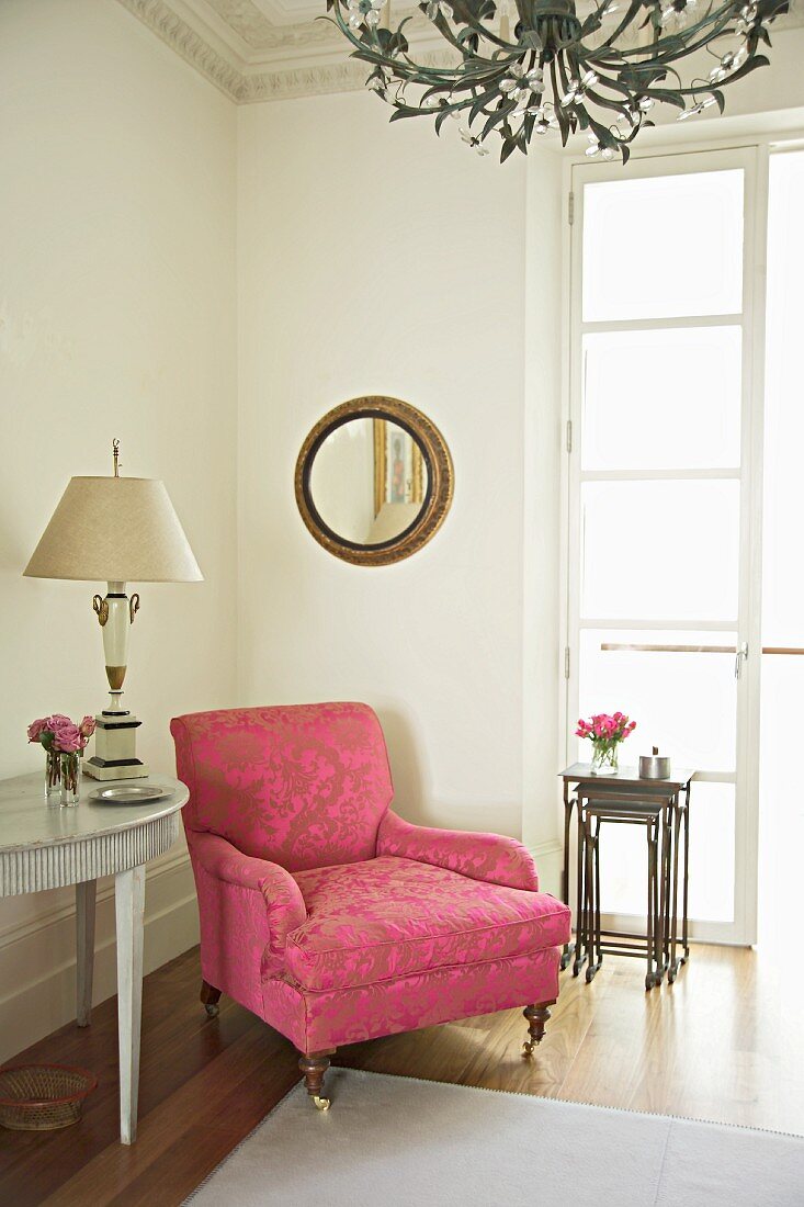 Antique armchair with ornamental pattern on pink brocade upholstery in corner of traditional room