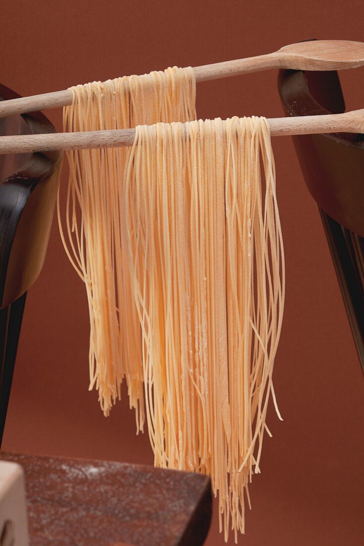 Pasta hanging from wooden spoons to dry