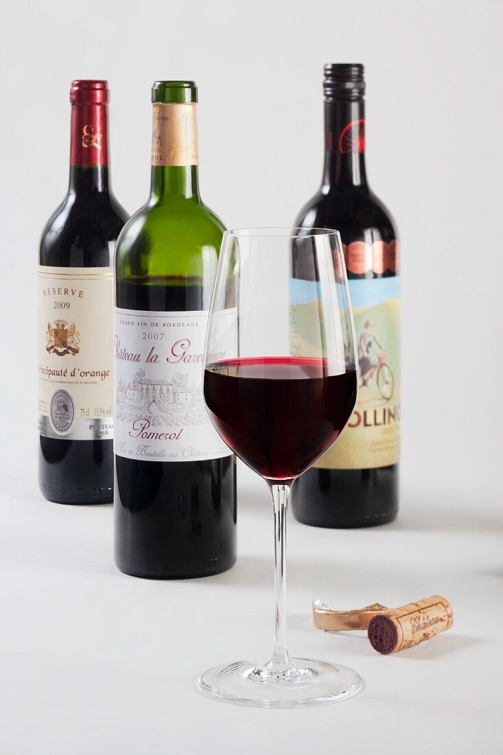 Ein Glas Rotwein vor Rotweinflaschen