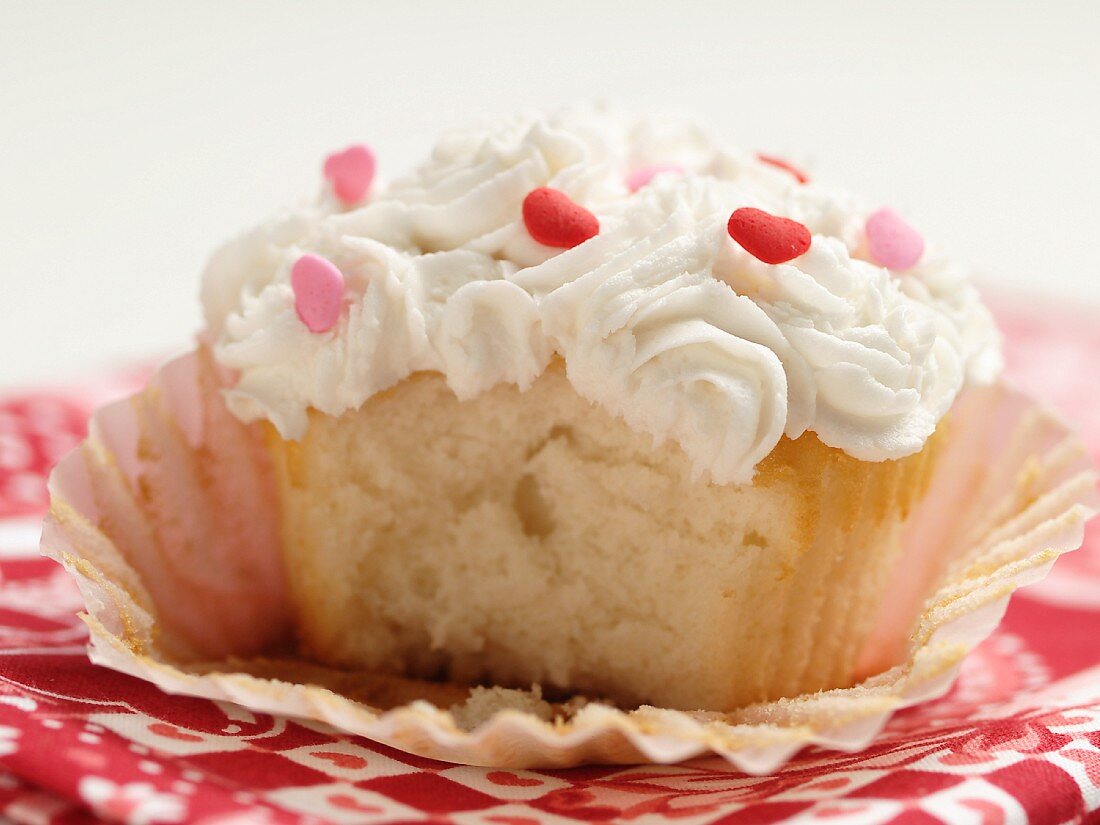 Cupcake mit Vanille-Topping und Zuckerherzen, angebissen