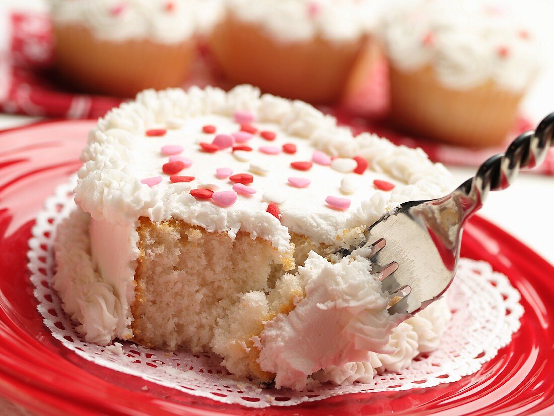 Kleiner herzförmiger Kuchen mit weißem Zuckerguss und Zuckerherzen