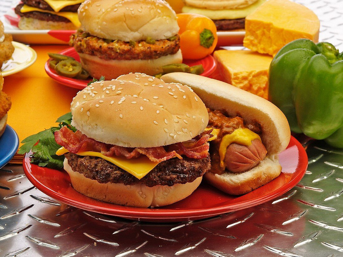 Cheeseburger mit Bacon und Hotdog, im Hintergrund Käse und Paprika