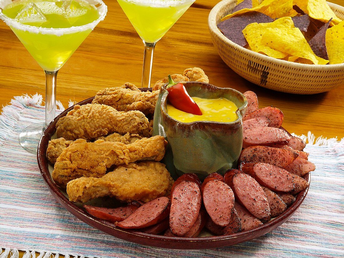 Mexikanische Vorspeisenplatte mit frittierten Hähnchenschenkeln und Wurst (Kielbasa), im Hintergrund Margaritas und Nachos