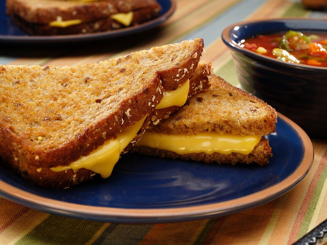 Getoastetes Käsesandwich auf blauem Teller mit Suppe im Hintergrund