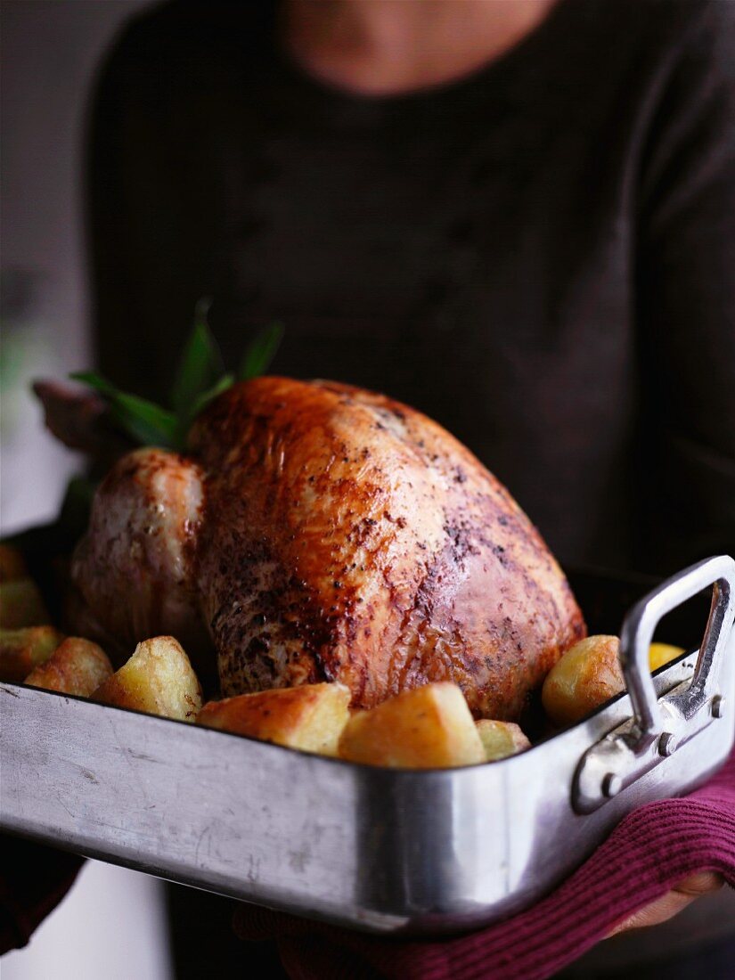 A woman holding a turkey and potatoes in a roasting tin