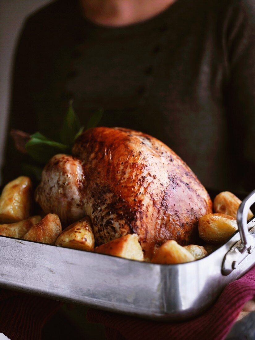 A woman a turkey and roast potatoes in a roasting tin