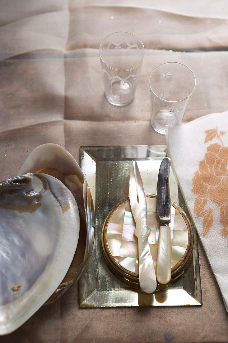 Cutlery with mother-of-pearl handles on silver dish next to large shell on table cloth