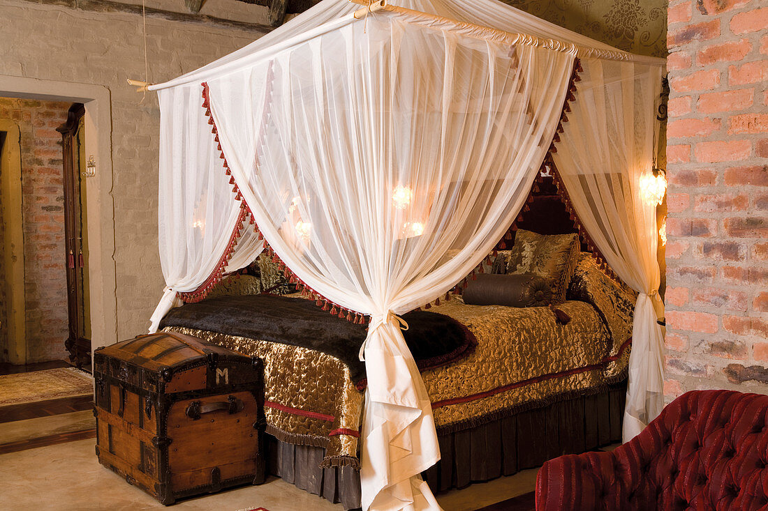 Four-poster bed with canopy and shiny gold bedspread in bedroom with exposed brick walls