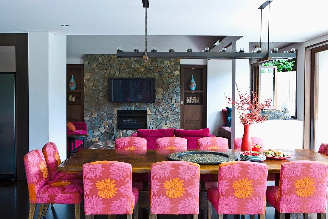 Upholstered chairs with patterned covers at dining table in front of open fireplace in stone wall