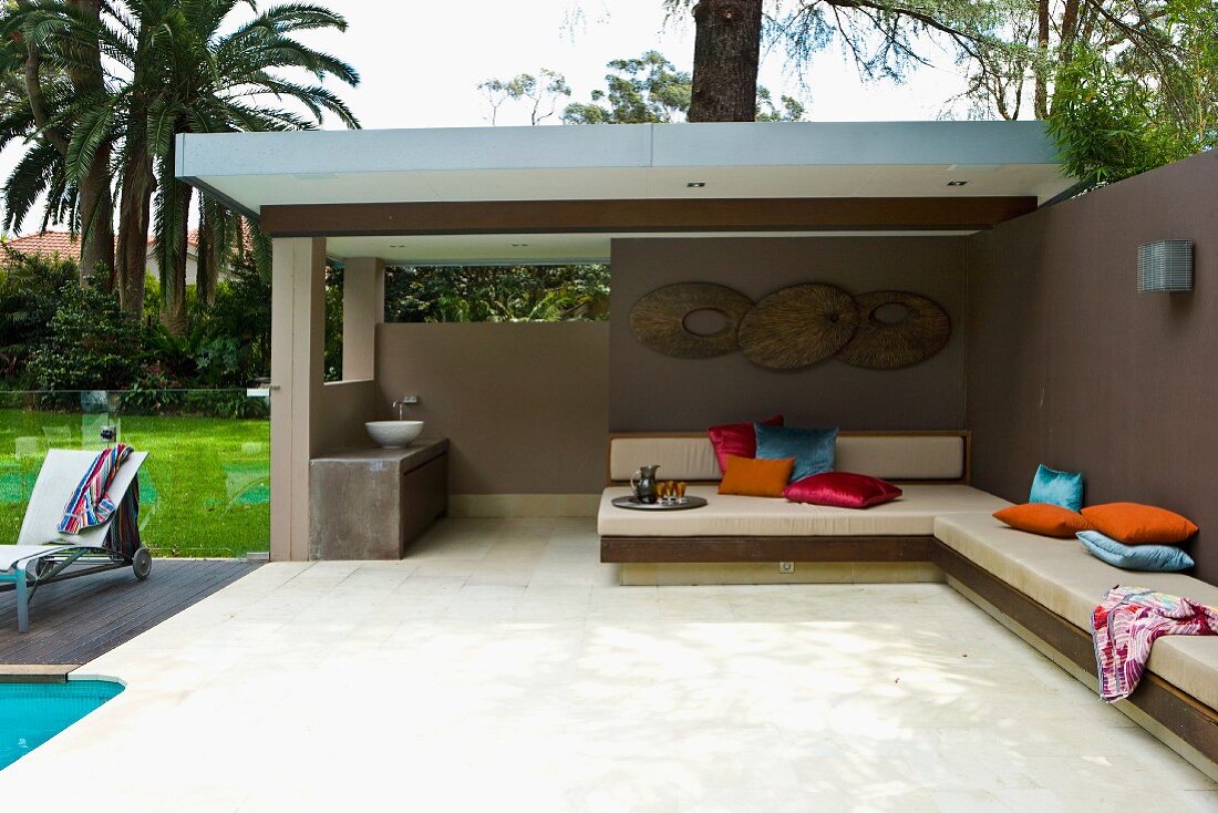 Partially roofed terrace in tropical garden with bench running along garden wall and around a corner