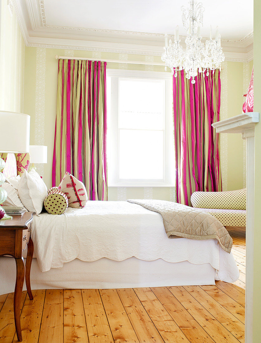 Cheerful pink and brown curtains in traditional bedroom with crystal chandelier and simple wooden floor