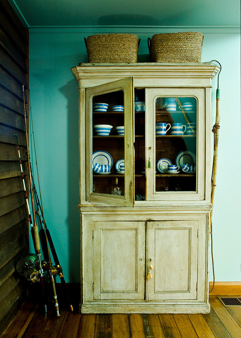 Glass fronted farmhouse dresser against turquoise-painted wall in corner of simple room
