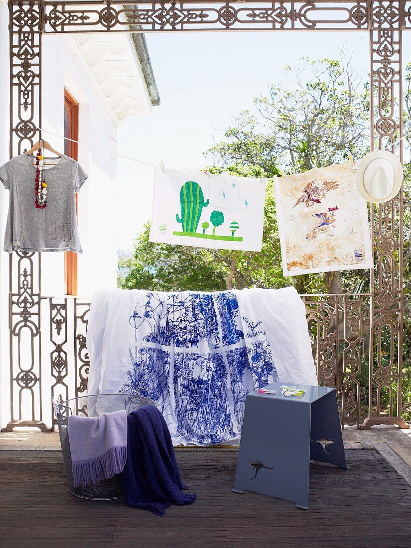 Veranda with decorative metal railings and textiles displayed from it; in front, a simple gray stool with a kangaroo shape carved into it