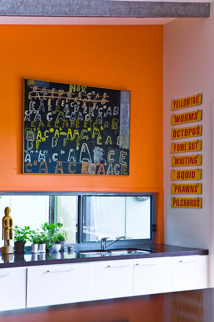 A corner of a kitchen with a bright orange wall and a large picture of letters