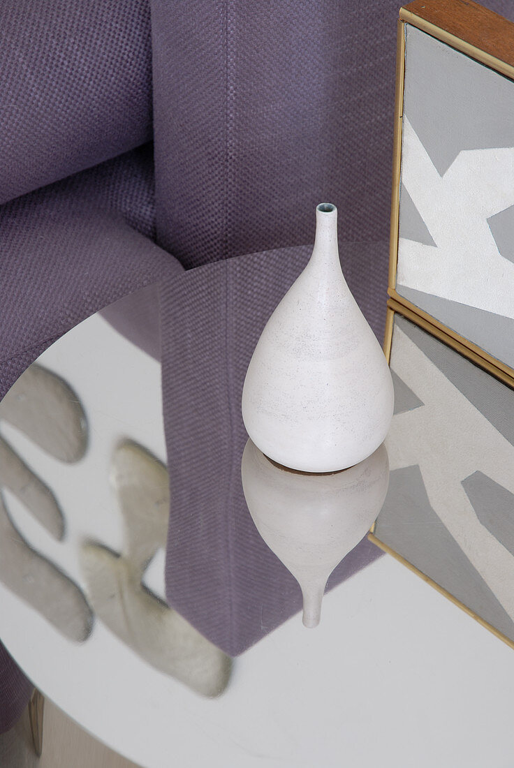 White ceramic vase on reflective side table in front of partial view of sofa