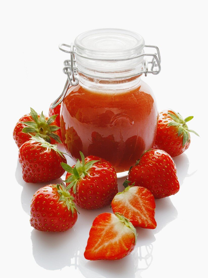 A jar of strawberry jam and fresh strawberries