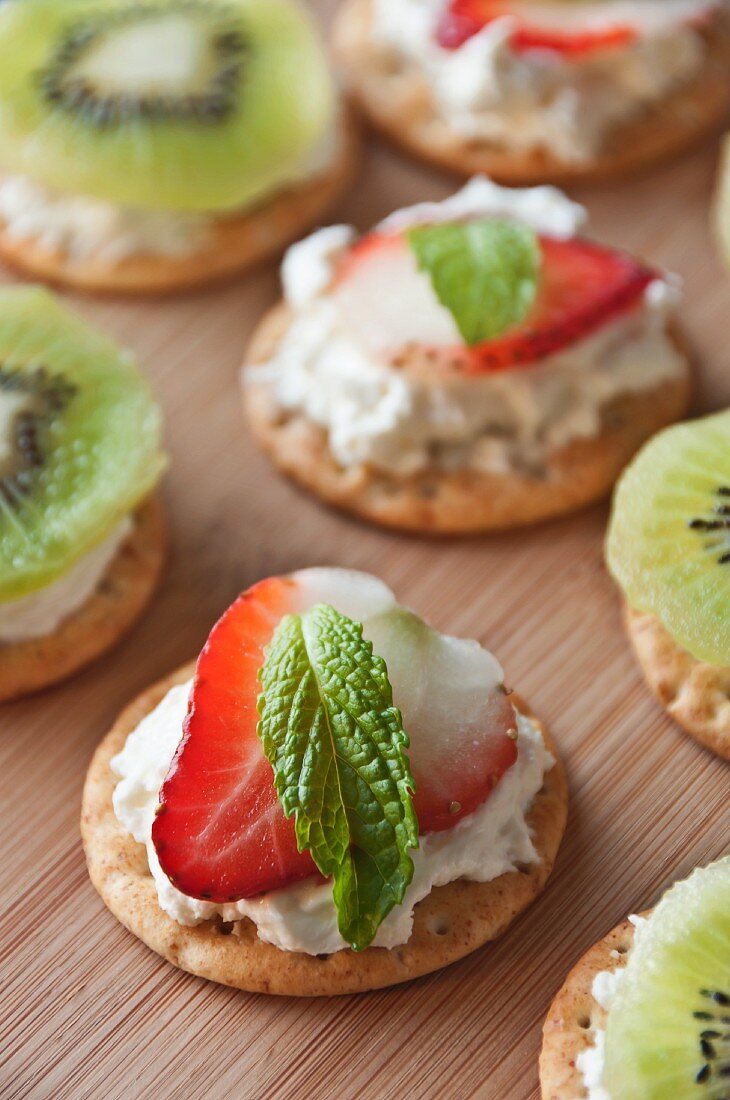 Crackers Topped with Cream Cheese, a Strawberry Slice and a Mint Leaf; Some Topped with Cream Cheese and Kiwi