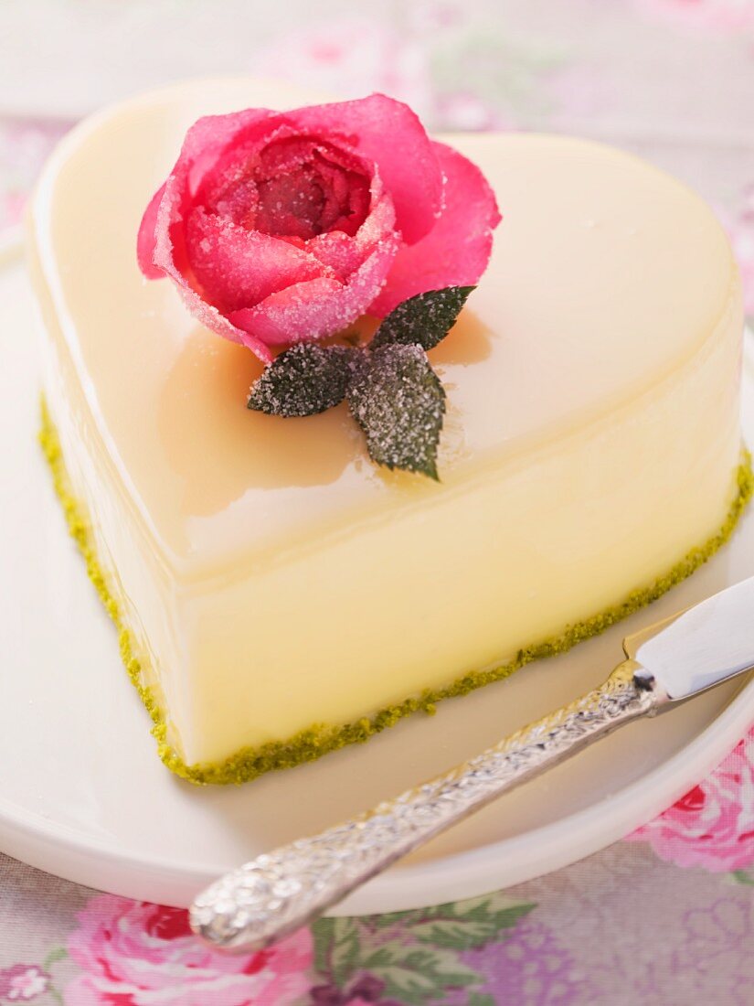 A heart-shaped cake with a white chocolate glaze and a sugared rose