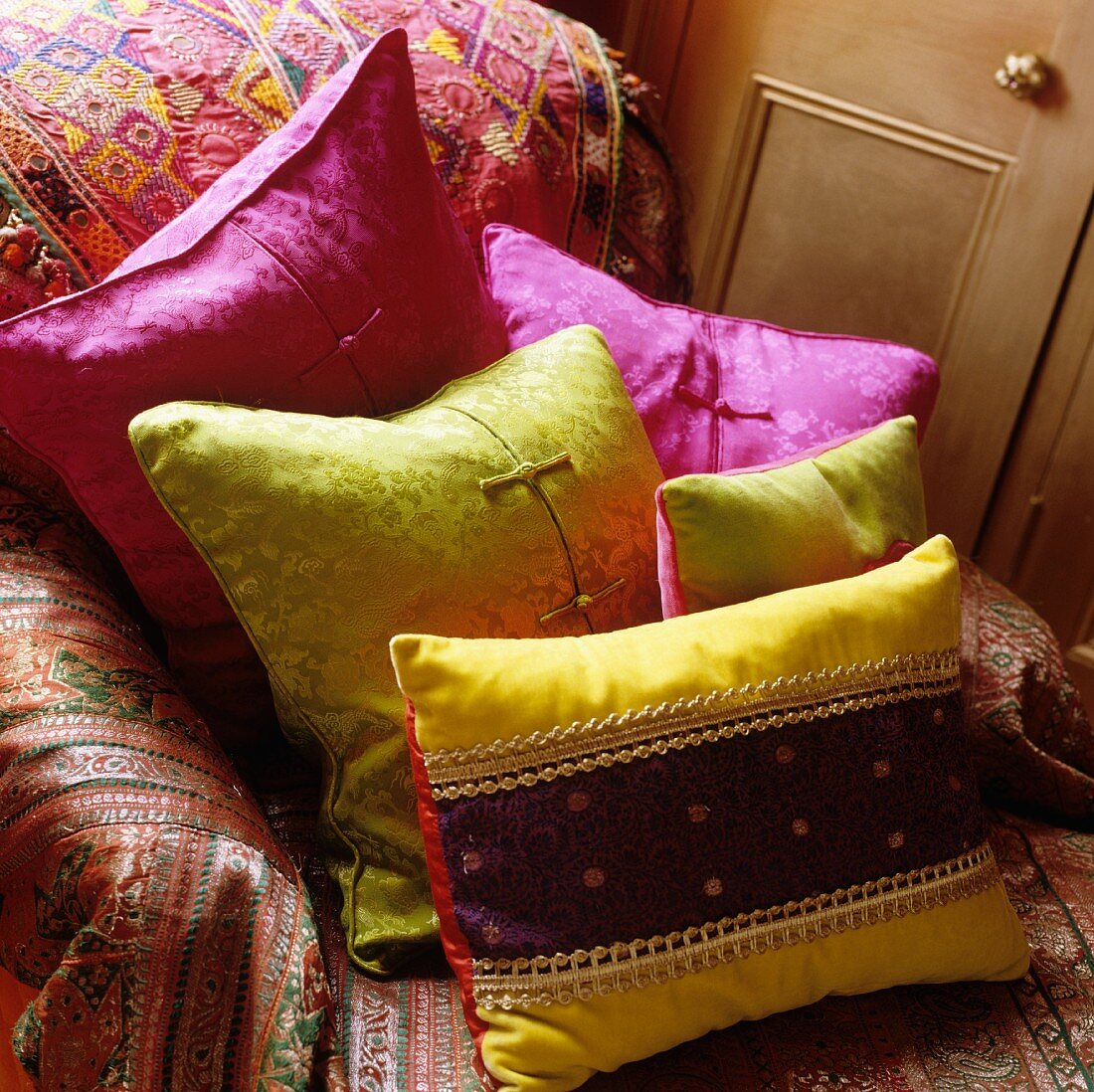 Farbenfrohe Satinkissen auf einem Sessel mit buntem Deckenüberwurf