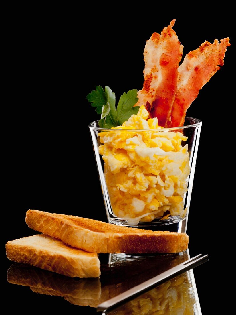 Scrambled egg with bacon in a glass with toast