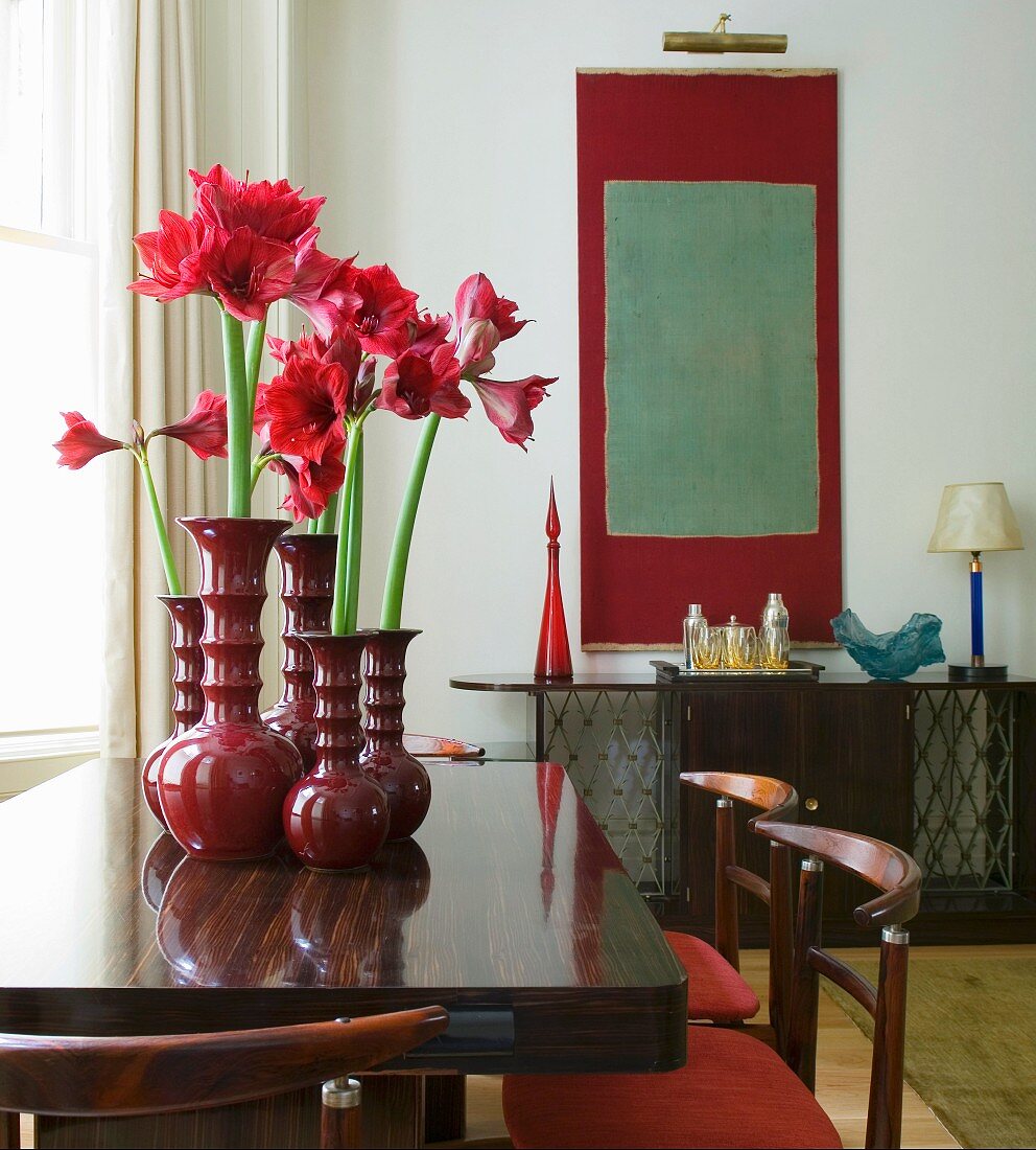 Rottöne in Esszimmer mit Retromöbeln - Amaryllis in dekorativen Keramikvasen und moderne Kunst im Hintergrund
