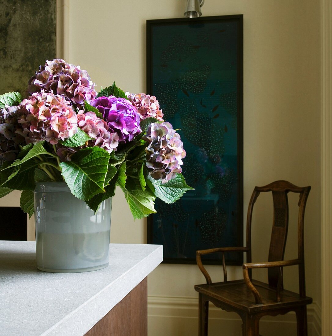 Bouquet of hydrangeas on kitchen counter; dark blue painting and antique wooden chair in background