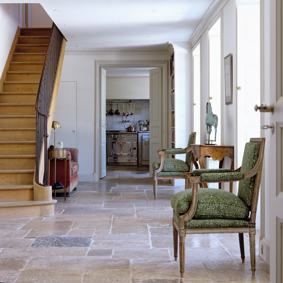 Antiker Stuhl mit Sitzpolster und alte Holztreppe im Vorraum eines mediterranen Landhauses mit Steinboden