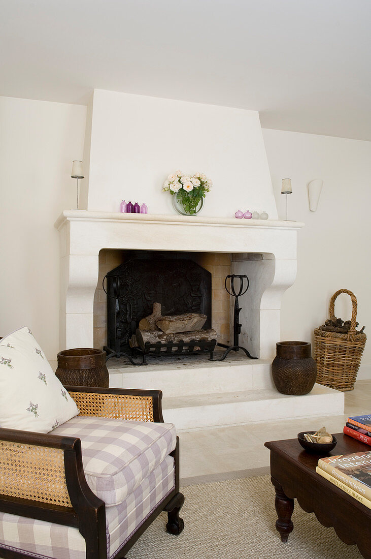 Traditional, upholstered wooden armchair with wickerwork panels and colonial coffee table in front of open masonry fireplace