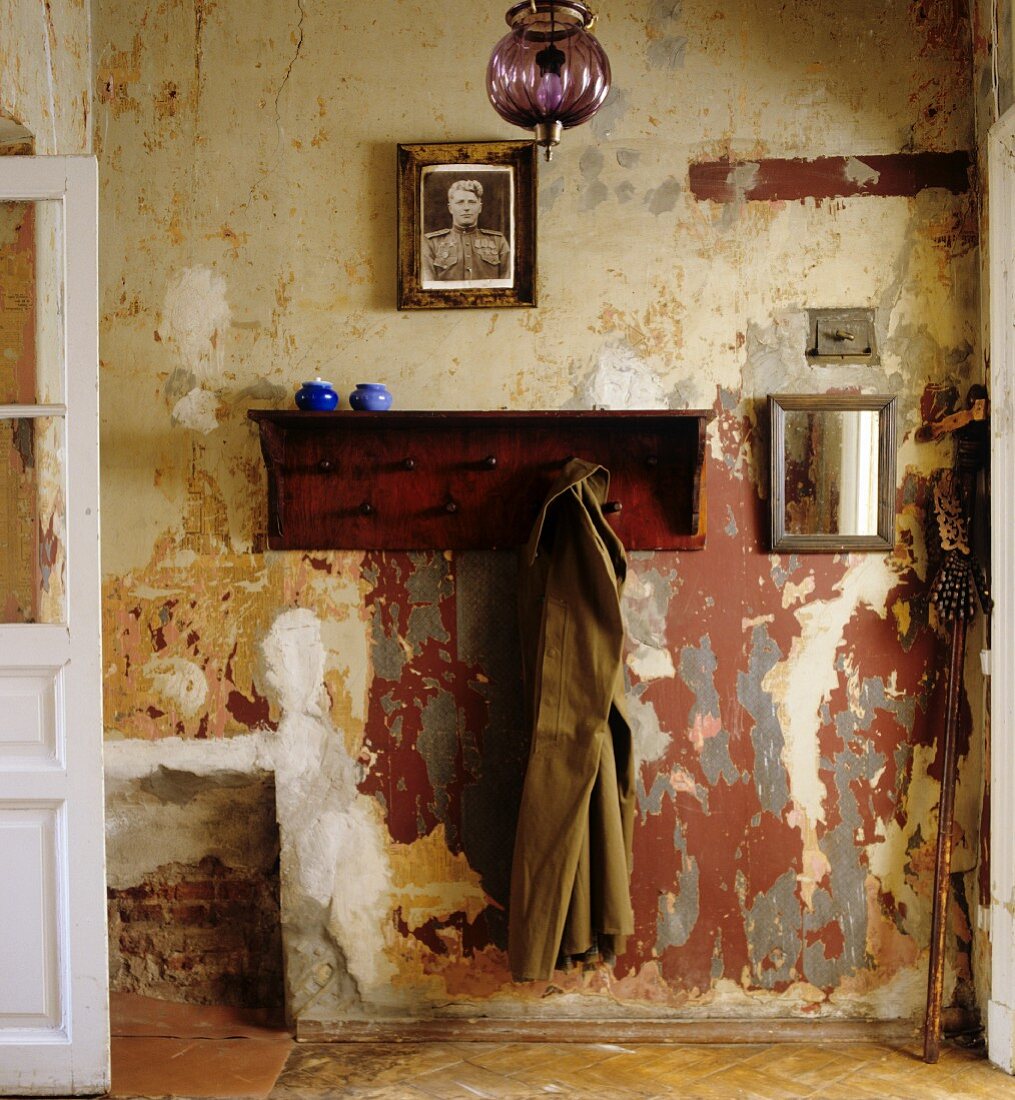 Offene Garderobe aus Holz mit aufgehängtem Mantel an Wand mit abblätternder Farbe in schlichtem Hausflur