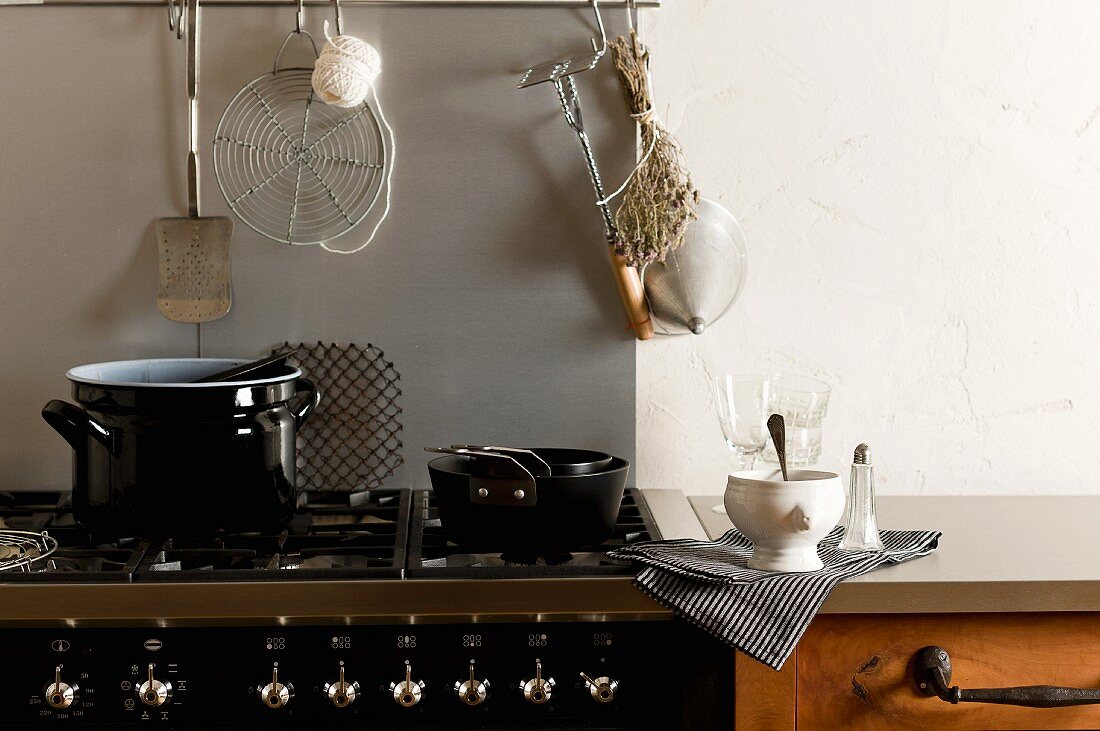 A kitchen counter with a cooker, pots and dried herbs