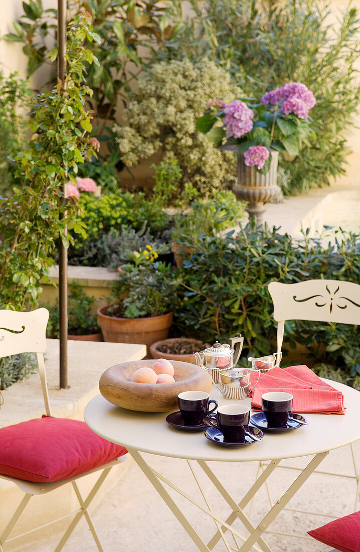 Frühstück auf Bistrotisch mit Stühlen aus weißem Metall und Pflanzentöpfe auf Terrasse