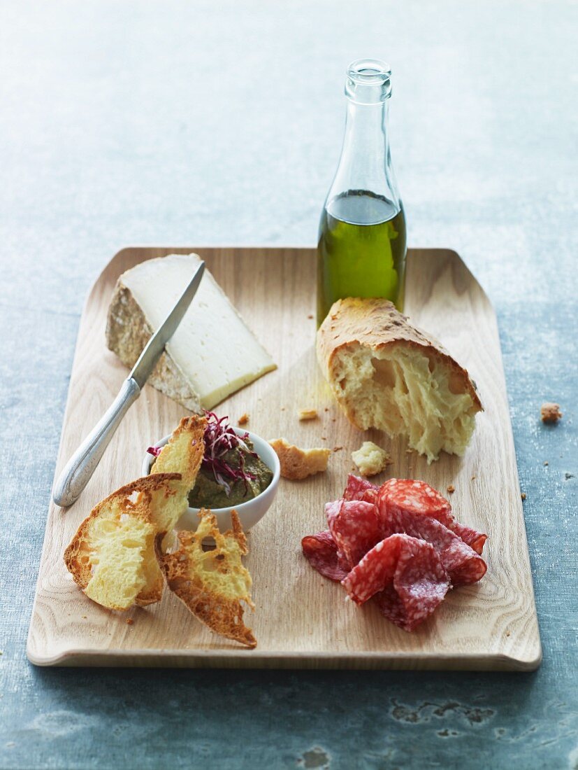 A board of appetizers with sausage, a dip, cheese and olive oil