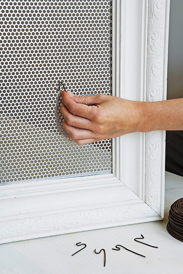 A picture frame being fitted with a wire mesh and hooks to store jewellery