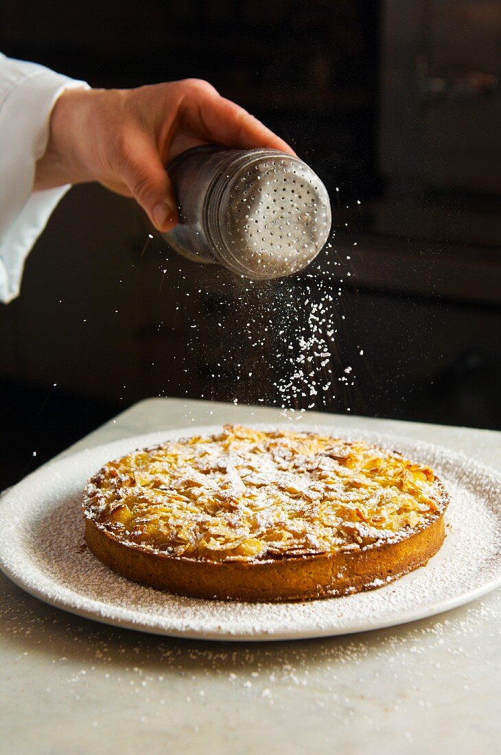 Apple tart being dusted with icing sugar