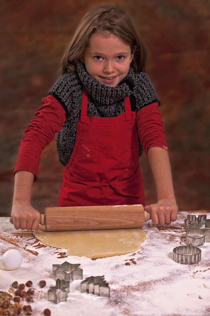 A girl rolling out biscuit dough with a rolling pin on a work surface