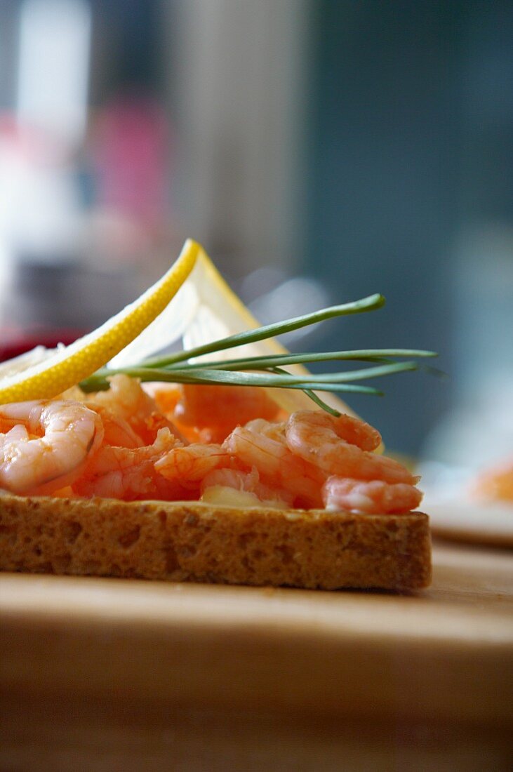 A slice of toast topped with prawns, lemons and chives
