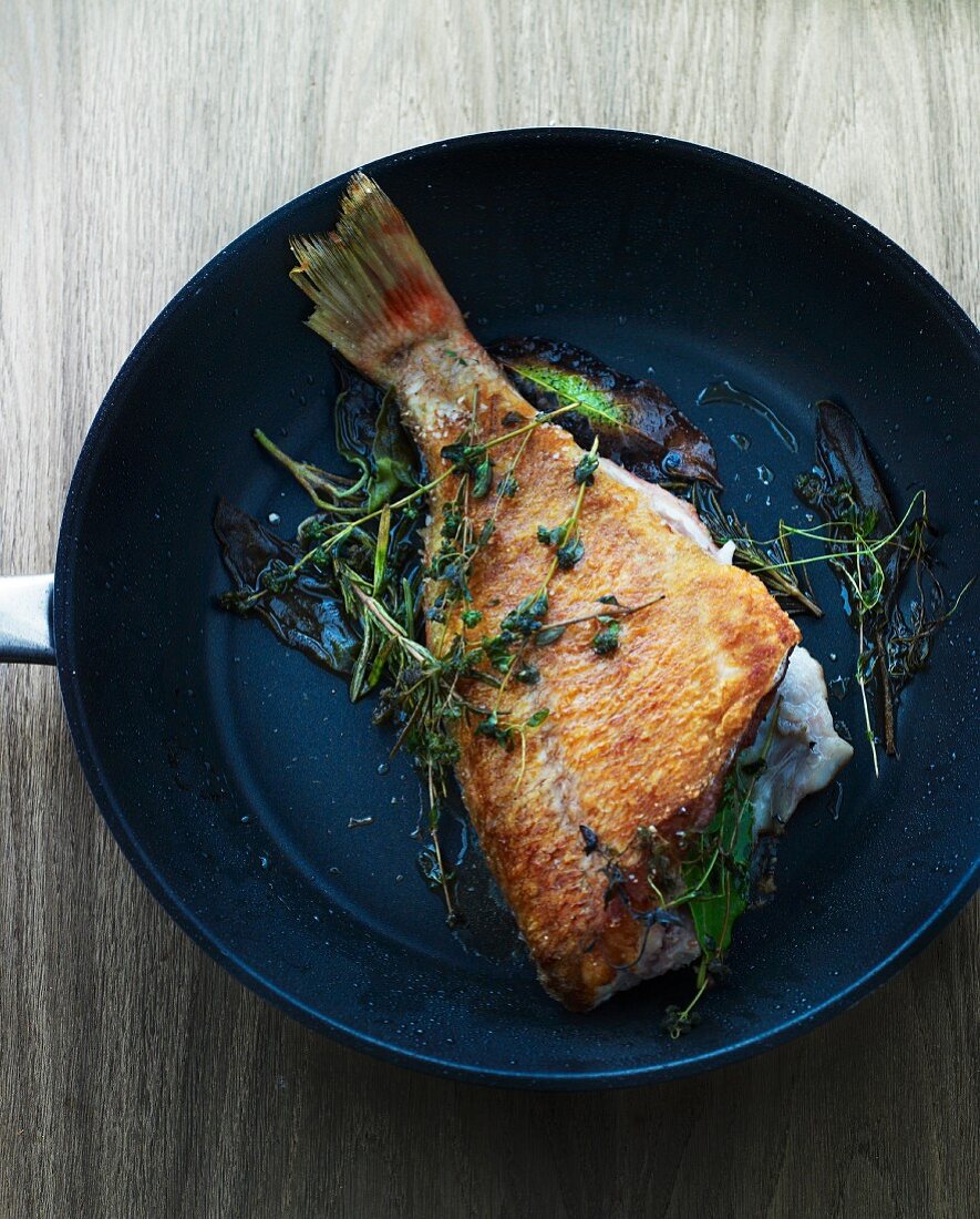 Fried fish with herbs in a pan (seen from above)