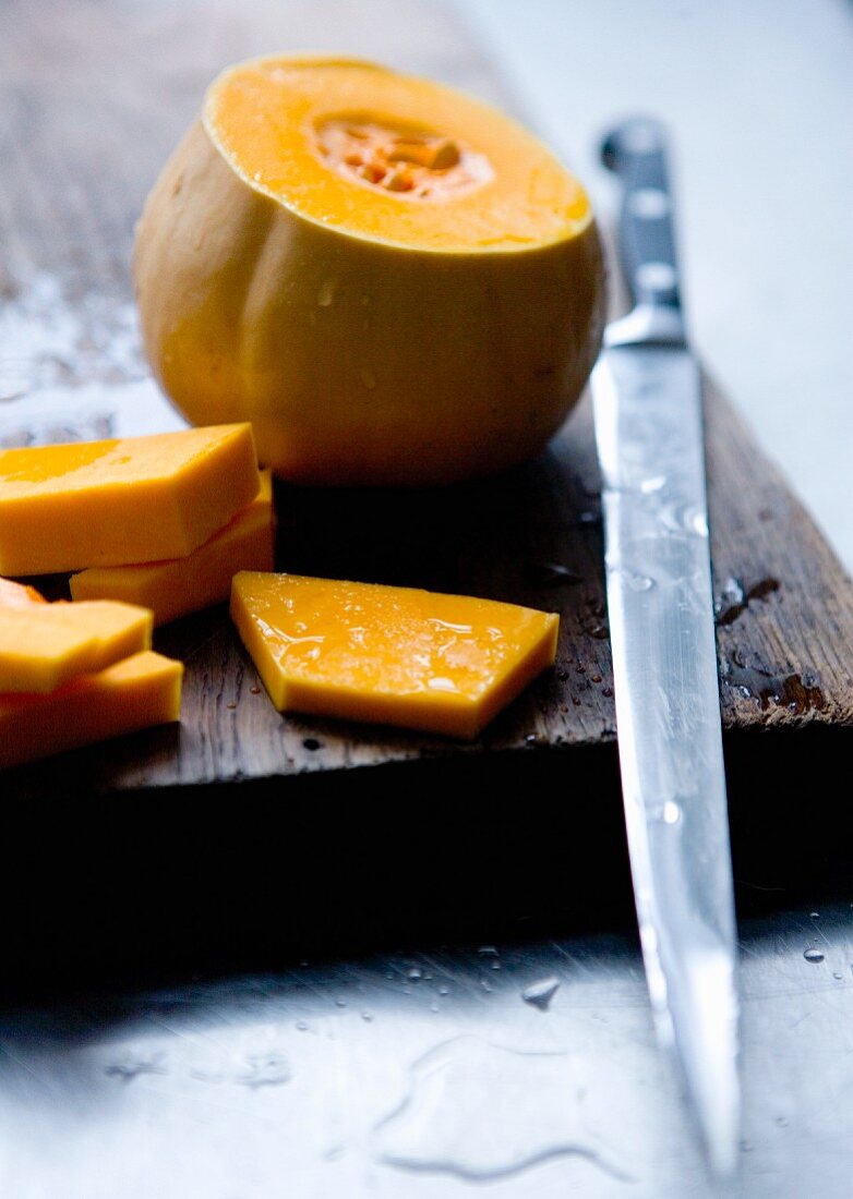 A sliced pumpkin with a knife on a wooden board