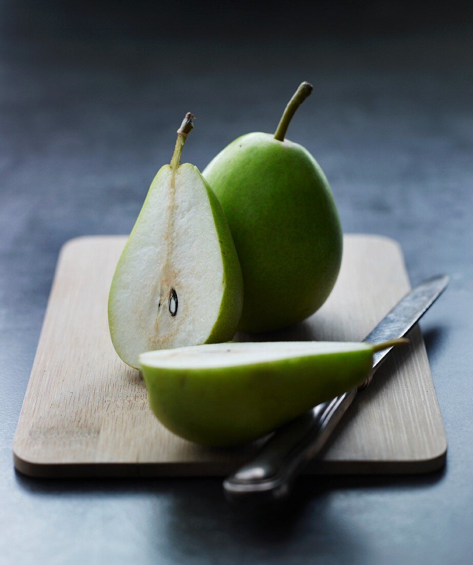 Two pears, whole and halved, on a wooden board with a knife