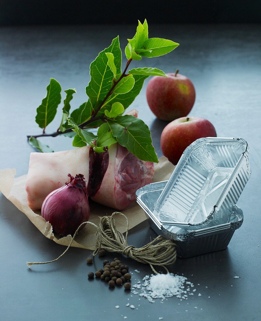 An arrangement of salted pork leg, apples, kitchen twine and aluminium containers