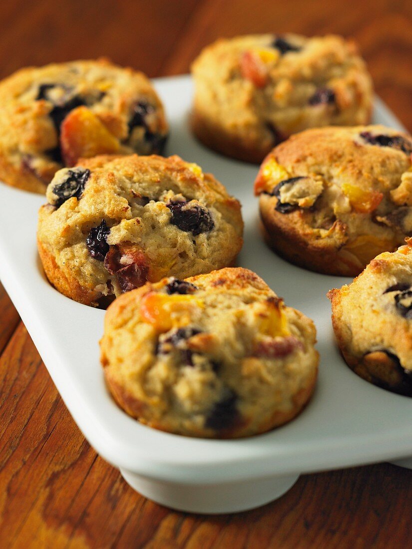 Blueberry and peach muffins in a muffin tin