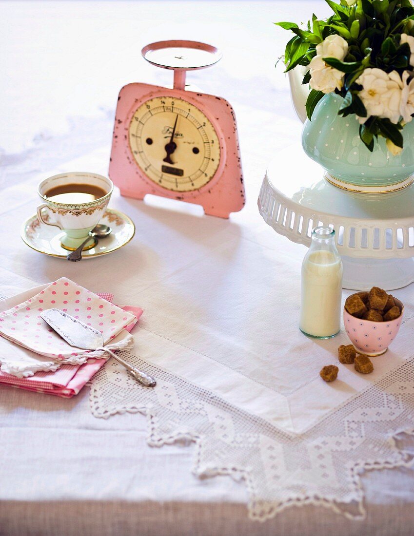 Eine Tasse Tee, eine alte Küchenwaage, Blumenstrauss, Kaffeesahne und brauner Zucker