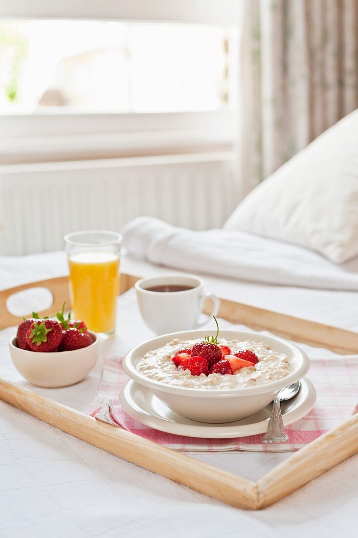 A breakfast tray on a bed (porridge with strawberries, coffee, orange juice)