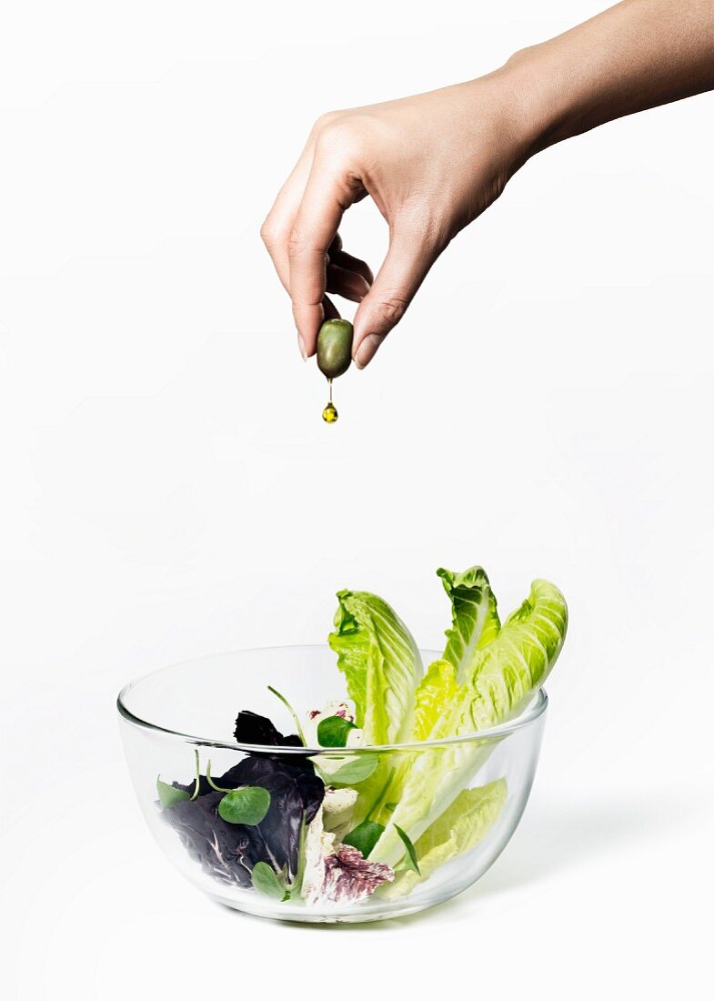 Hand presst Olivenöl aus Olive auf Blattsalat