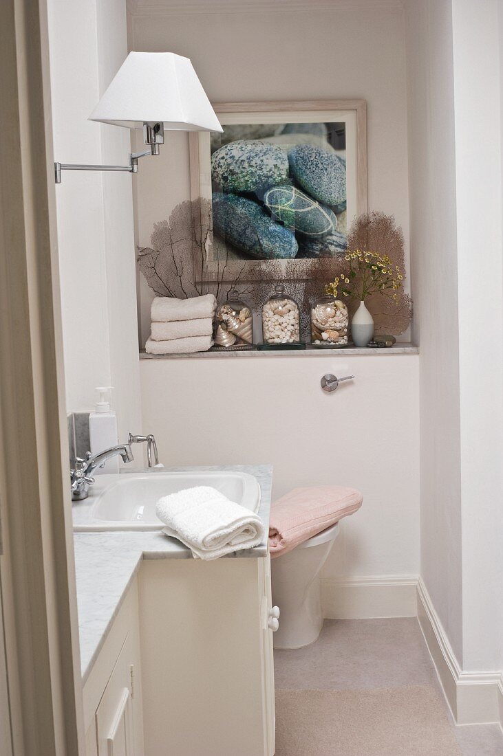 Classic bathroom with marble washstand and seashell arrangements on shelf below framed picture