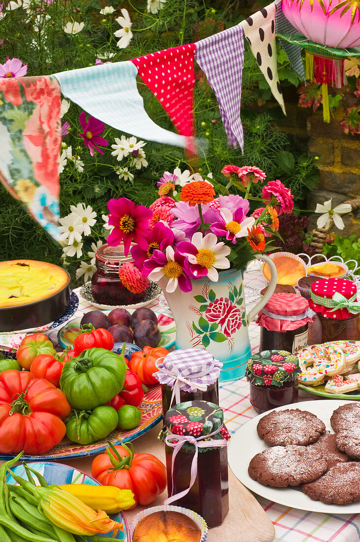 Gedeckter Tisch mit Plätzchen, frischem Gemüse, Marmeladen und Kuchen im Garten