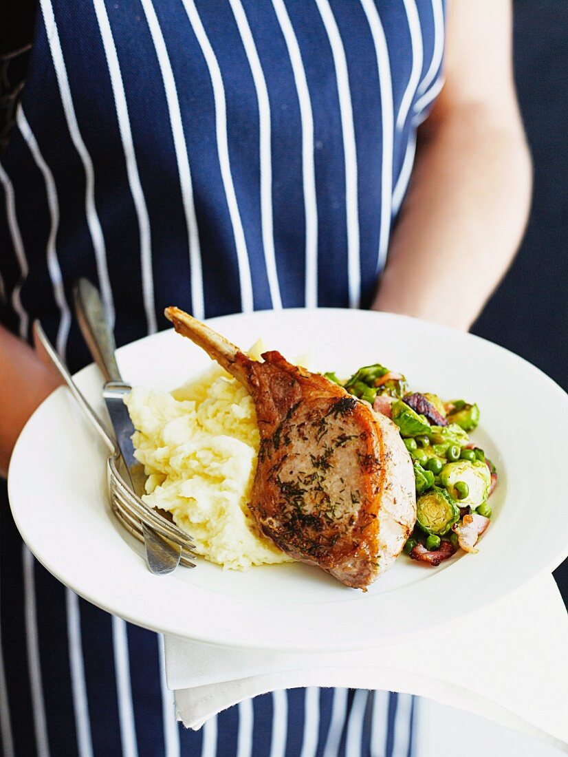 A pork chop with bacon, Brussel sprouts, peas and mashed potatoes