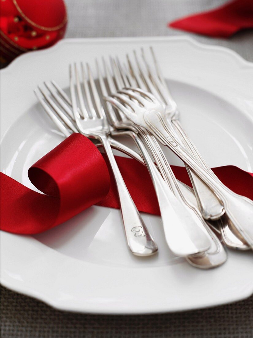 Weisser Teller mit Gabeln und rotem Geschenkband