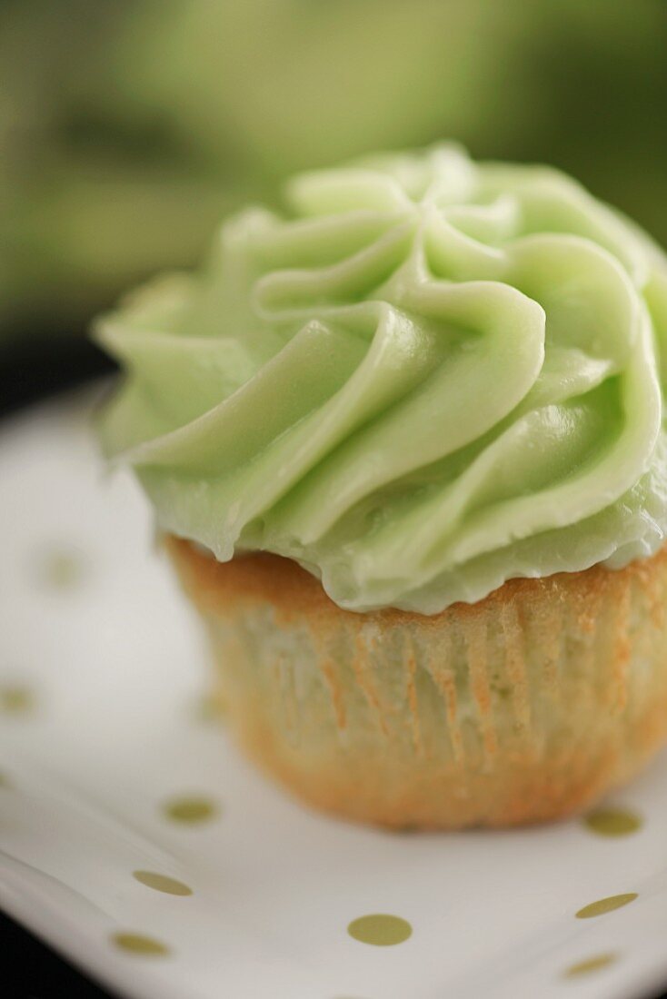 Cupcake mit grüner Creme auf gepunktetem Teller